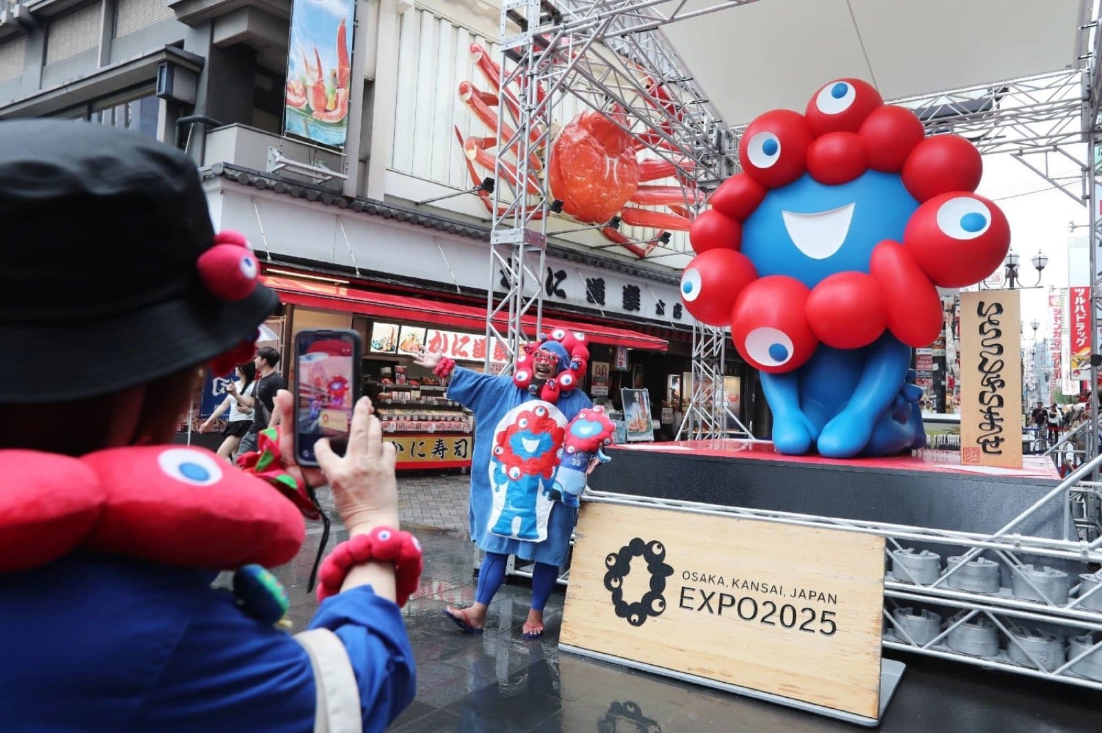 Tourists pose with the Osaka Expo 2025 mascot on a shopping street in Osaka