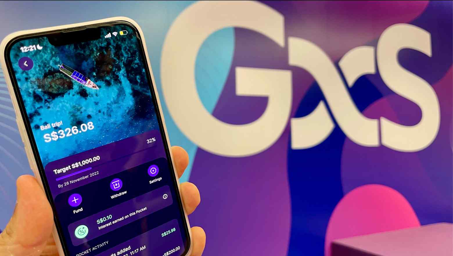 A hand holding a smartphone showing a GXS Bank savings pocket, in front of the GXS logo