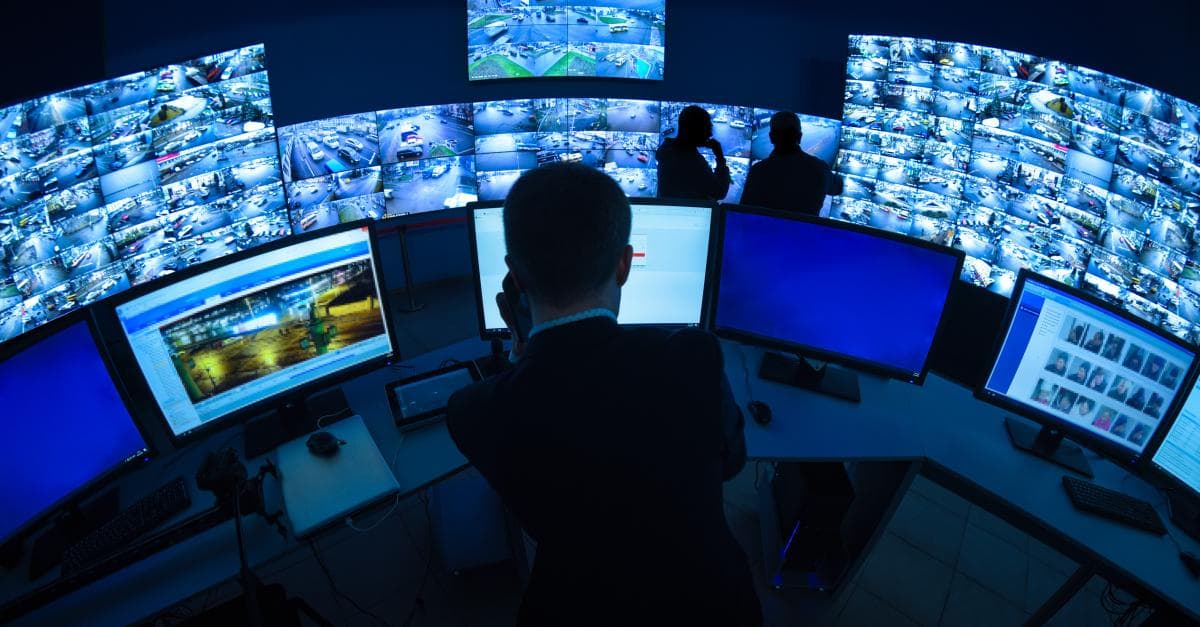 A security operator monitors a wall of live camera feeds in a control room