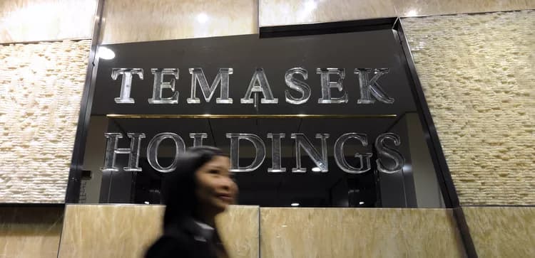 A woman walks past an illuminated Temasek Holdings sign at the company's offices