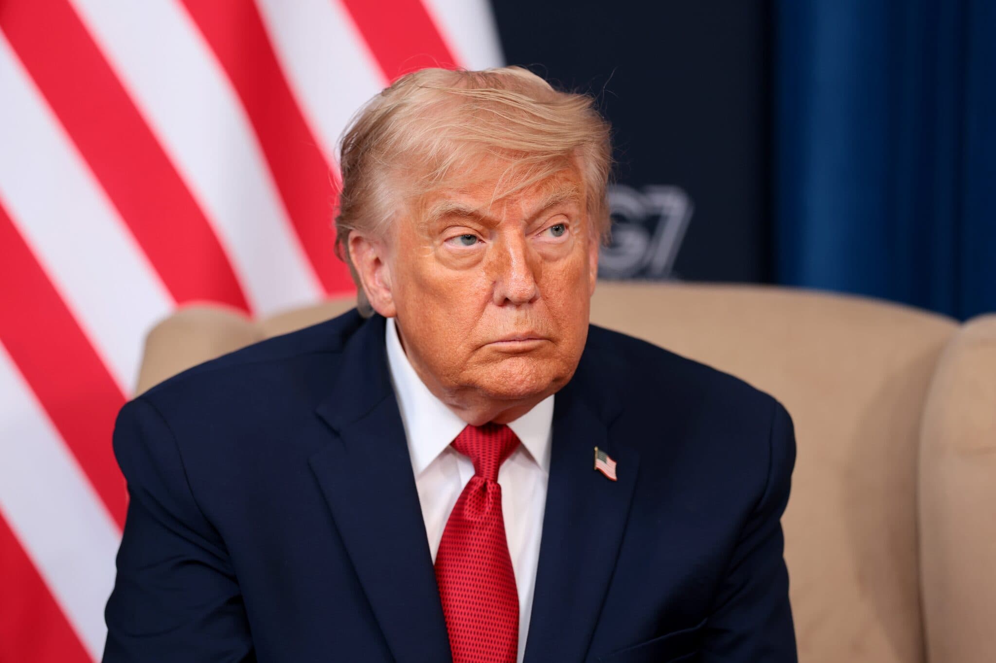 Donald Trump sits in front of an American flag at a G7 event