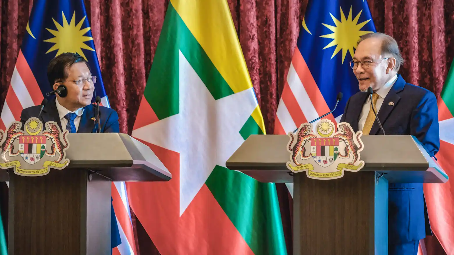 Malaysian Prime Minister Anwar Ibrahim and a Myanmar official speaking at podiums in front of their countries' flags