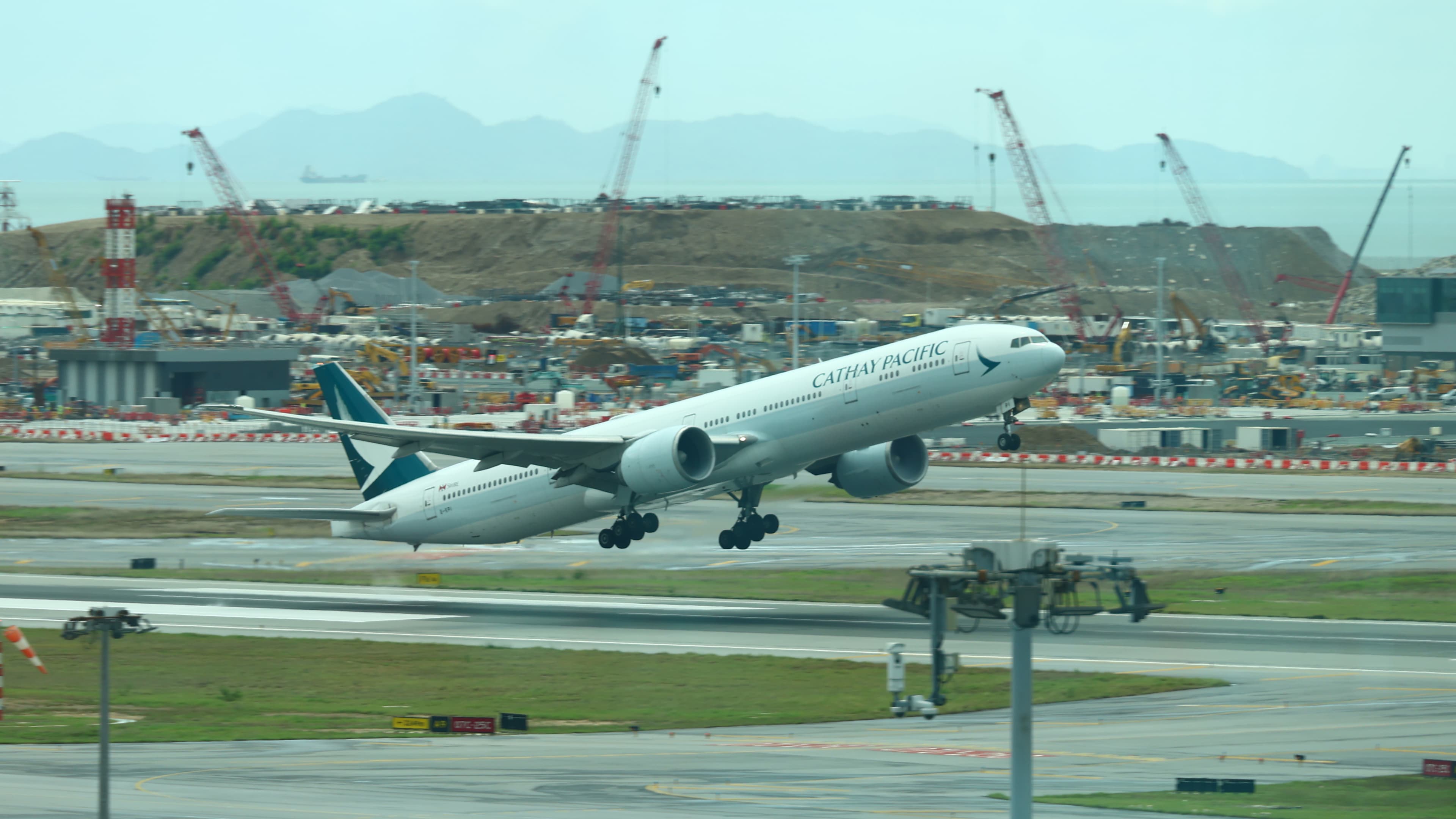 A Cathay Pacific Boeing 777 taking off from Hong Kong International Airport with construction cranes in the background