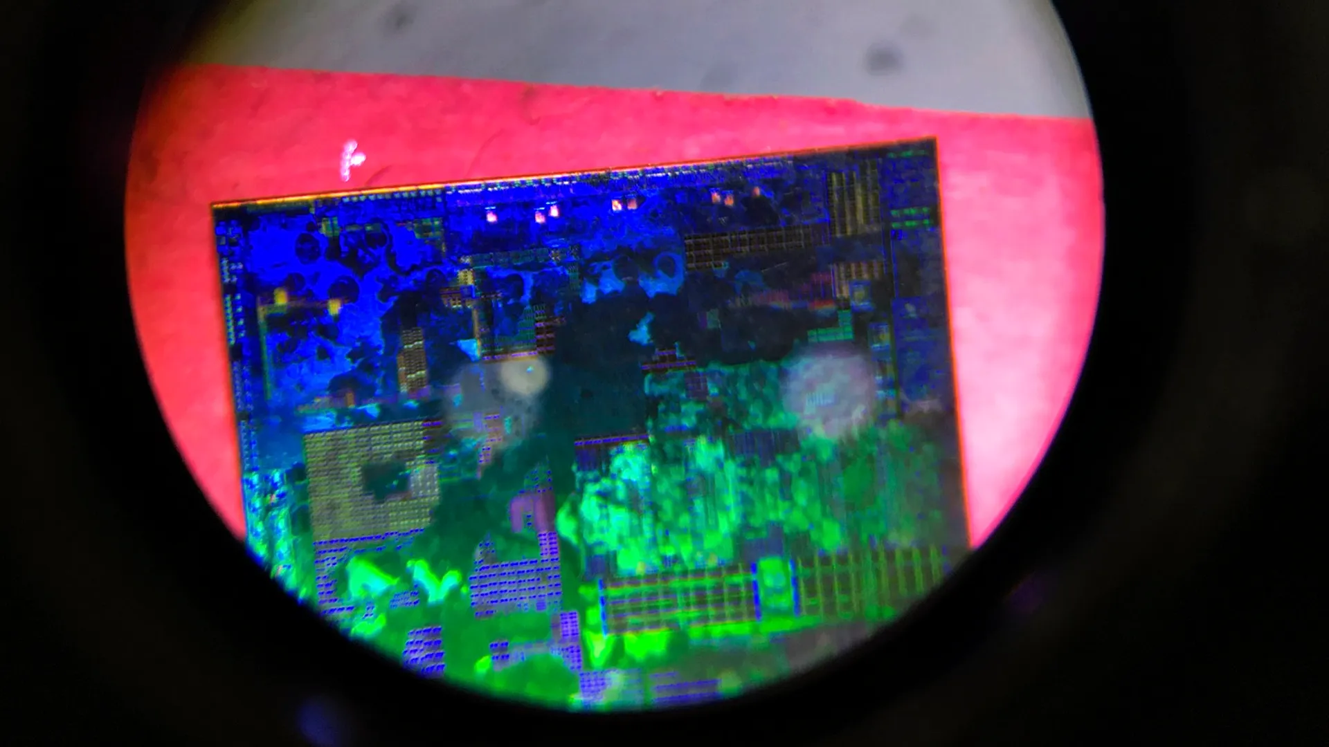 A semiconductor chip die viewed through a microscope, lit in blue and green