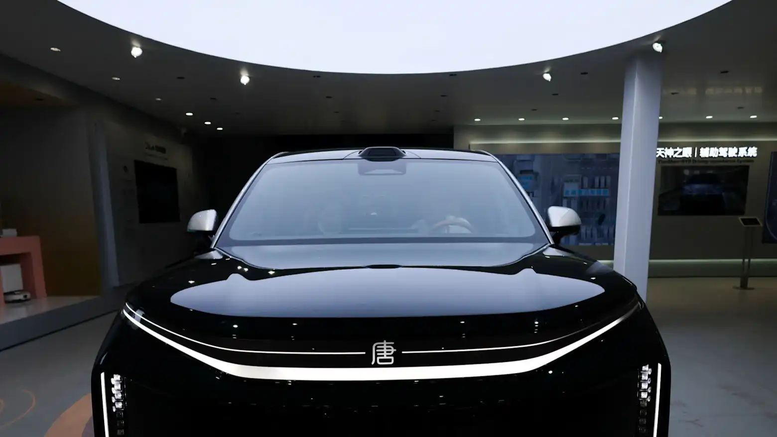 The front grille and windshield of a black BYD Tang electric SUV on a showroom floor