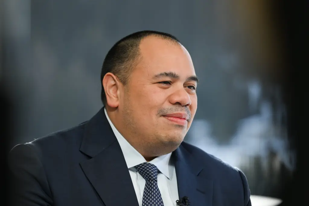 A smiling man in a dark suit and patterned tie being interviewed on stage