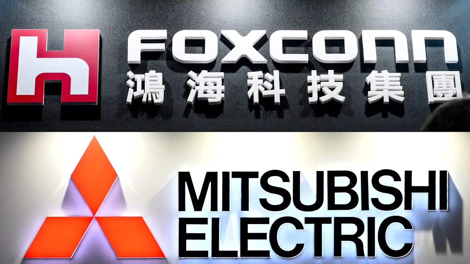 Foxconn and Mitsubishi Electric company logos and signage stacked on a dark background