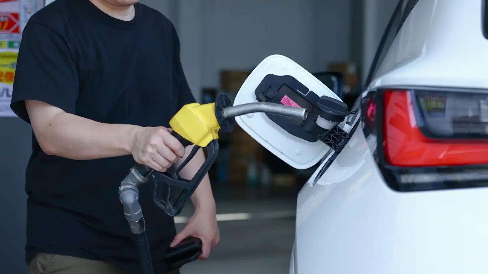 A person fueling a gasoline car parked next to an electric vehicle being charged