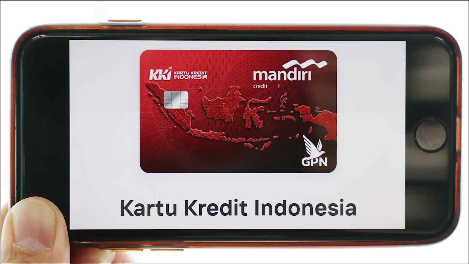 A hand holds a phone displaying a red Kartu Kredit Indonesia (KKI) credit card issued by Bank Mandiri with the GPN logo