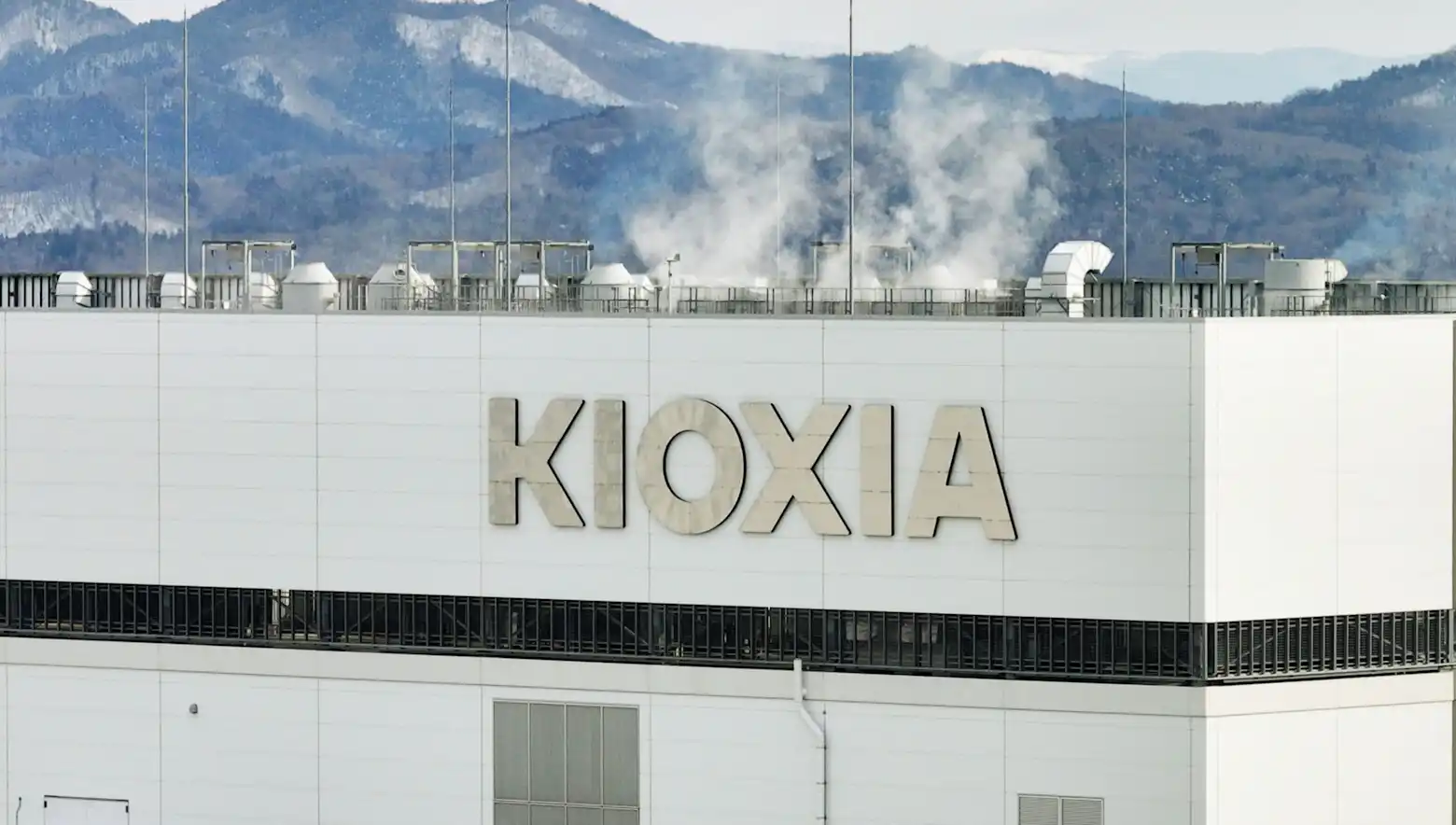 The Kioxia logo on the exterior of a memory chip plant, with snow-dusted mountains behind it