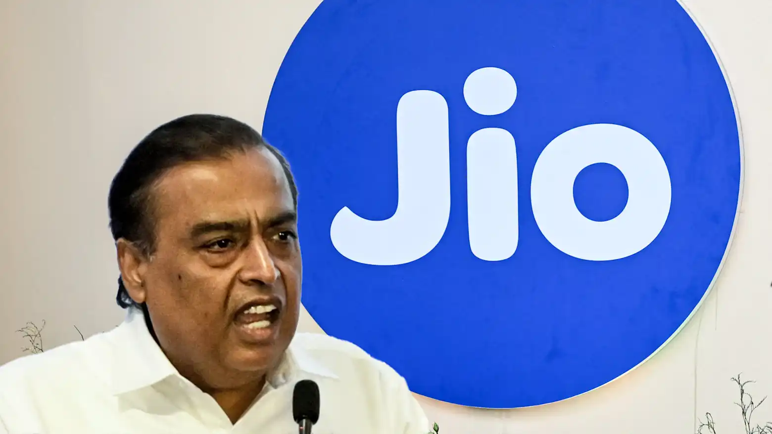 Mukesh Ambani speaking at a microphone in front of a large Jio logo