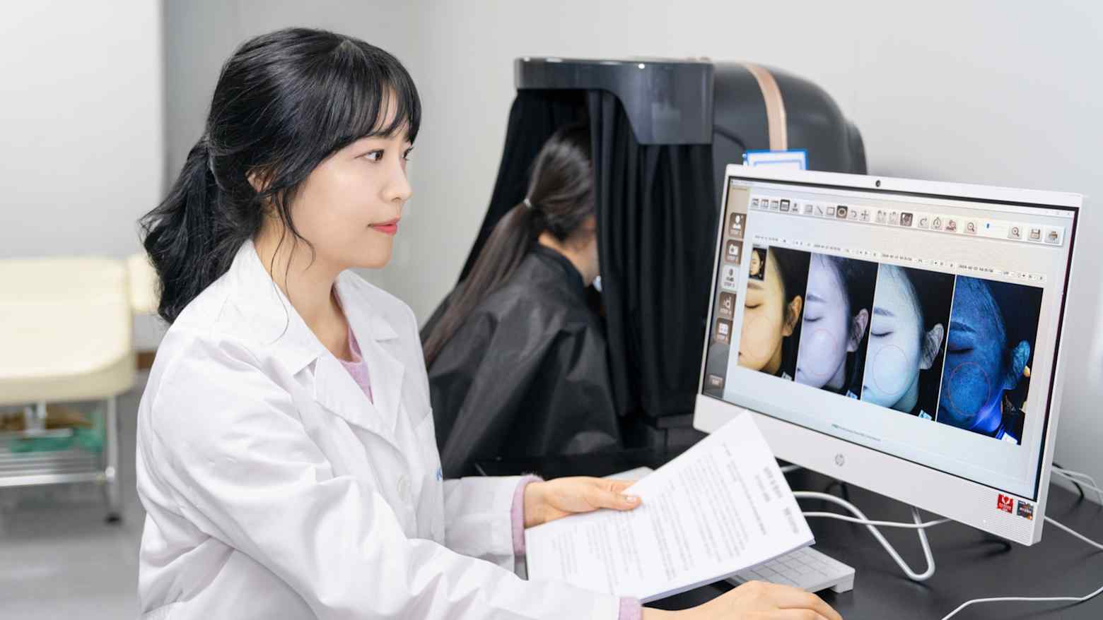 A researcher in a white coat reviews skin analysis images on a screen at a cosmetics contract manufacturer's lab