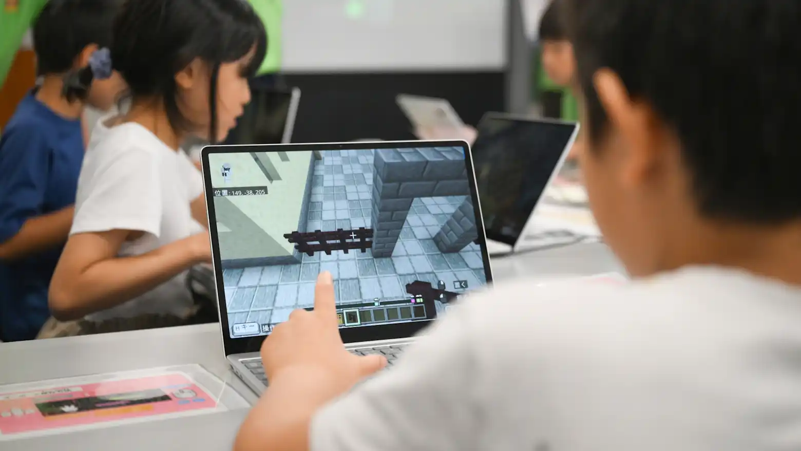 A student points at a Minecraft reconstruction of a prewar Tokyo streetscape on a laptop screen