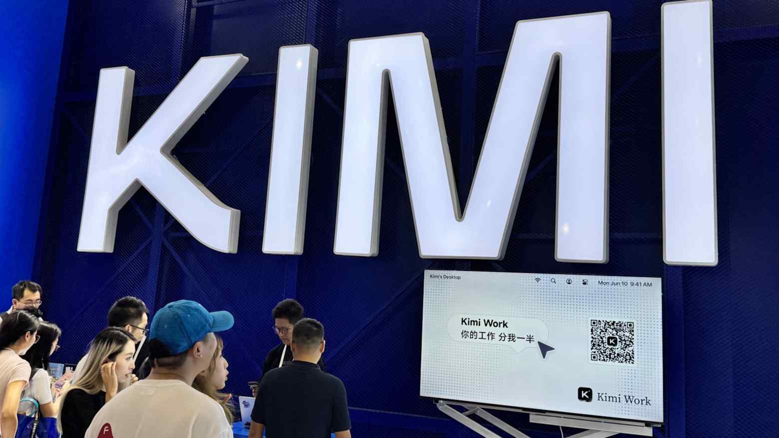 Visitors gather at Moonshot AI's Kimi booth, with a large illuminated KIMI sign and a screen showing Kimi Work