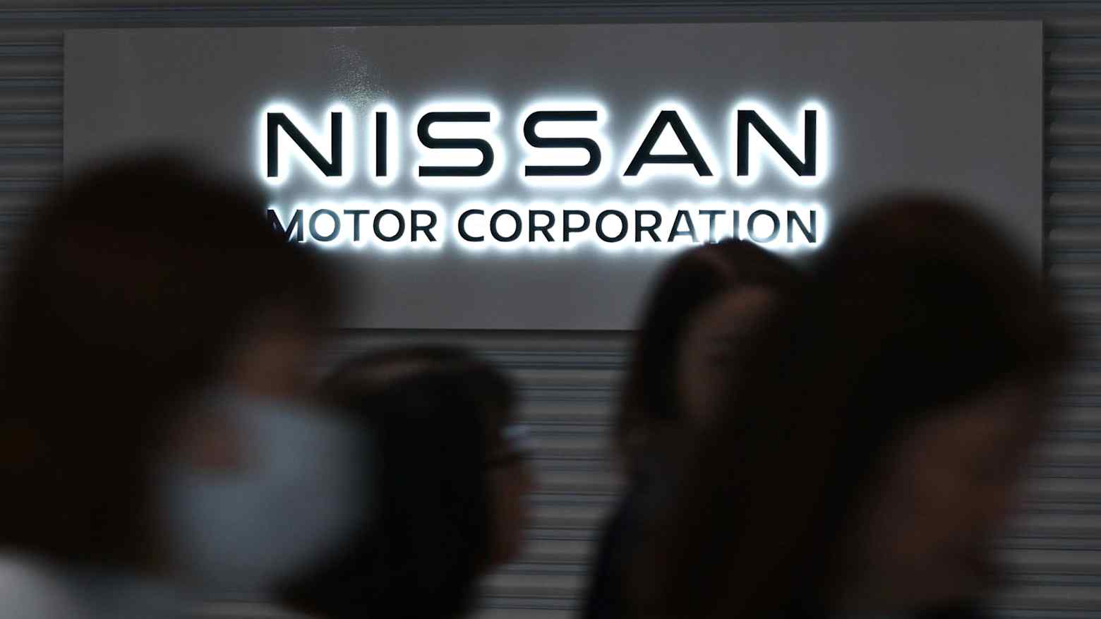 People walk past an illuminated Nissan Motor Corporation logo sign