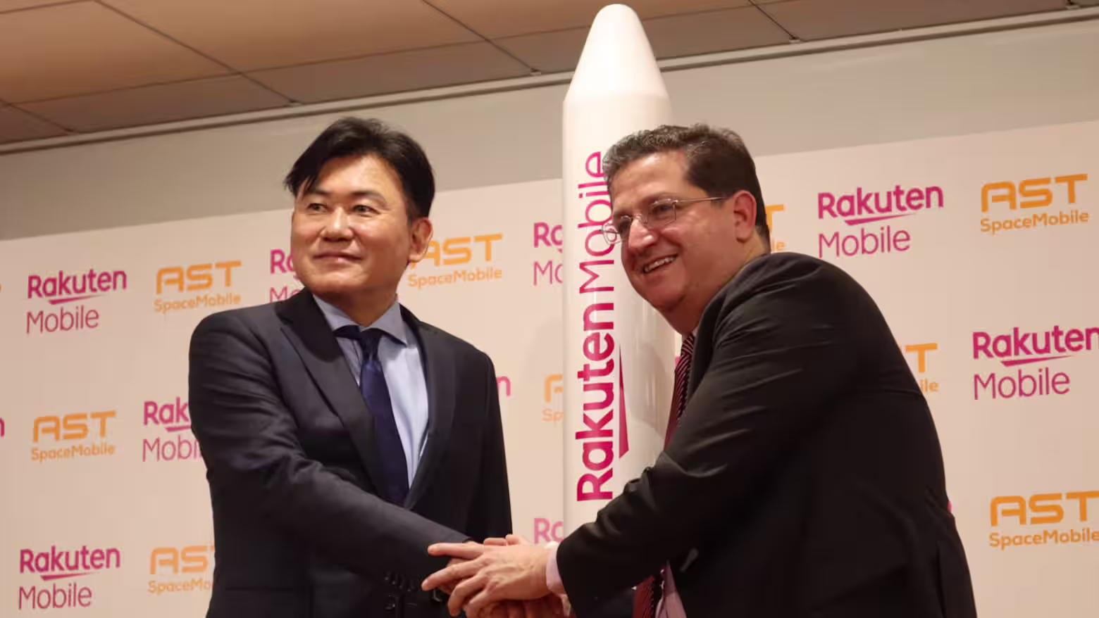 Rakuten Group and AST SpaceMobile executives shaking hands in front of a satellite mockup