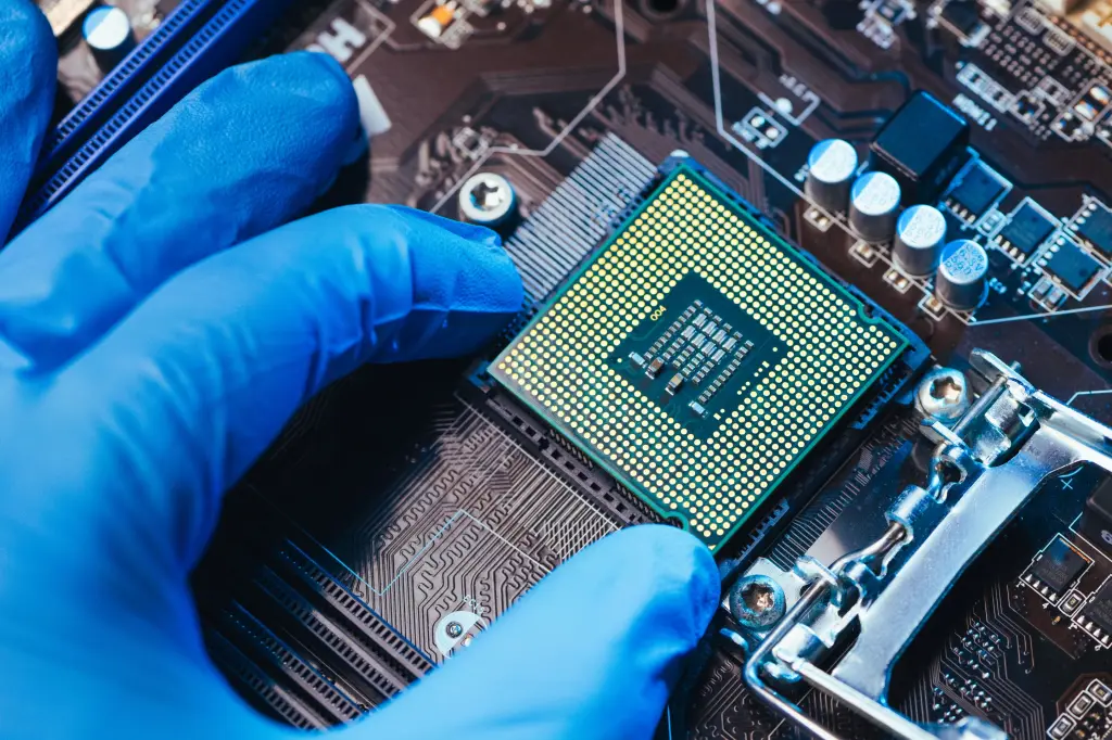 A gloved hand placing a semiconductor chip onto a circuit board socket