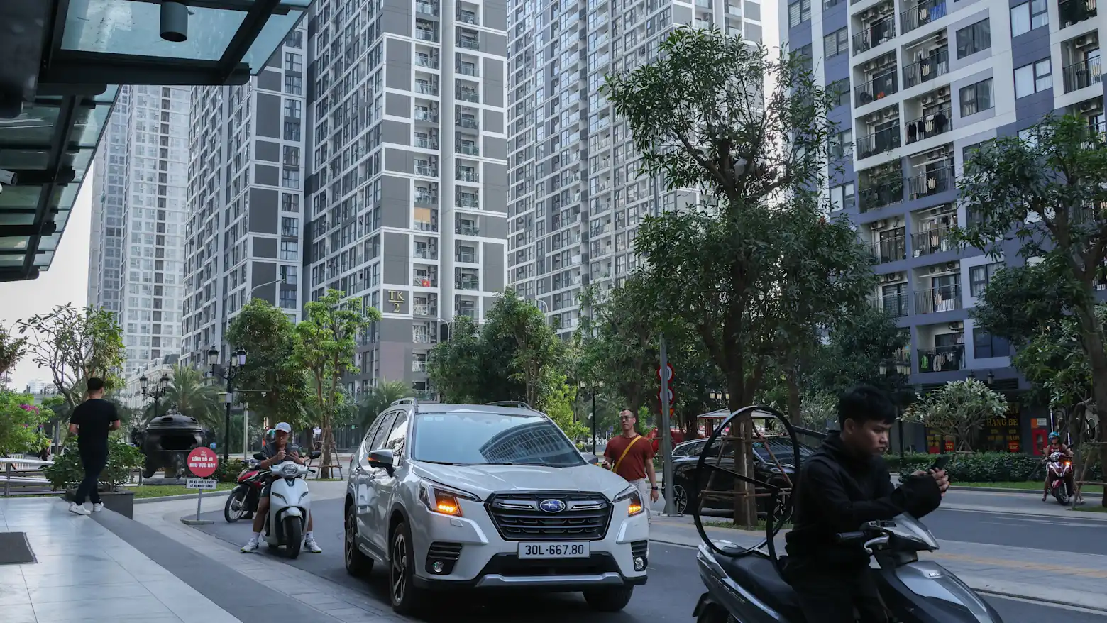 A street lined with high-rise apartment towers in Hanoi, with cars, motorbikes, and pedestrians passing by